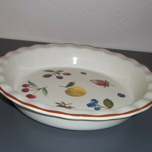 May include: White ceramic pie dish with a scalloped edge and a brown rim. The interior features a colorful fruit design, including cherries, blueberries, a lemon, and a strawberry. A decorative and functional kitchenware item.