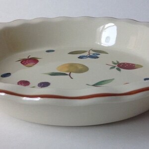 May include: Off-white ceramic pie dish with a scalloped edge and a brown rim. The interior features painted illustrations of strawberries, blueberries, and a yellow fruit. A decorative kitchenware item.