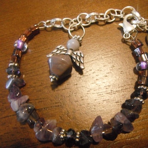 May include: A purple and brown beaded bracelet with a silver angel charm and a silver ribbon charm with the word "HOPE" on it.