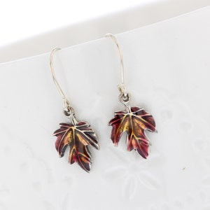 May include: A pair of silver dangle earrings with red, orange, and yellow enamel maple leaf charms.