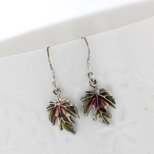 May include: A pair of silver dangle earrings with green, red, and brown enamel maple leaf charms.
