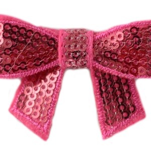 Puede incluir: Un lazo rosa hecho de lentejuelas. El lazo est&aacute; cosido con hilo rosa.