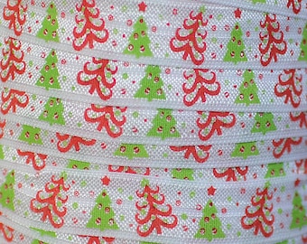 May include: White elastic hair tie with a repeating pattern of red and green Christmas trees. The trees are outlined in white and have a white star on top.