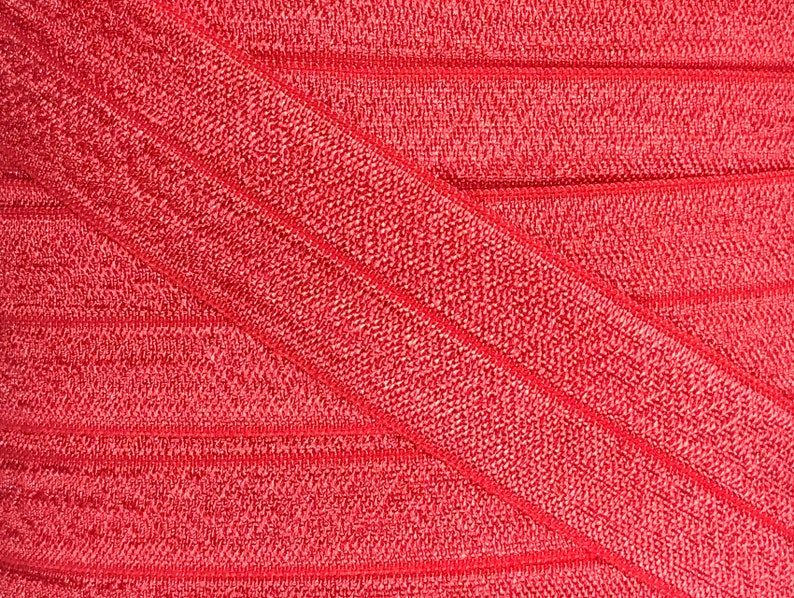 K&ouml;nnte beinhalten: Roter elastischer Stoff mit einer strukturierten, gerippten Oberfl&auml;che. Der Stoff ist in der Mitte gefaltet und erzeugt ein diagonales Muster.