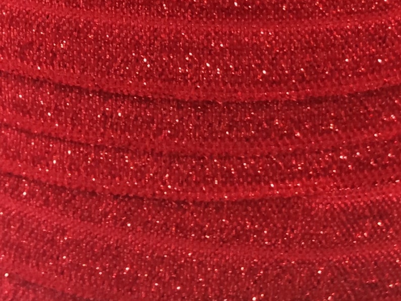 May include: Red glitter fabric with a textured, woven pattern. The fabric is folded in a series of overlapping layers.