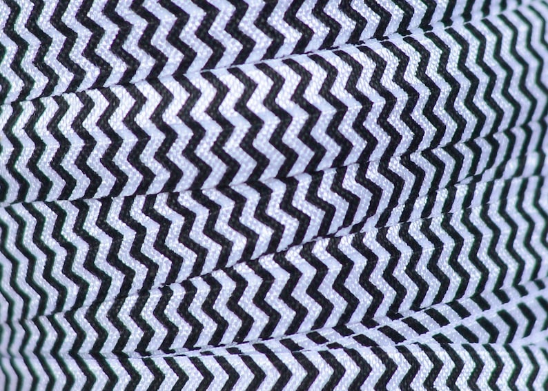 Op de afbeelding: Zwart-wit geblokt elastisch met een zigzagpatroon. Het elastisch is gevouwen en toont het patroon dat zich herhaalt.