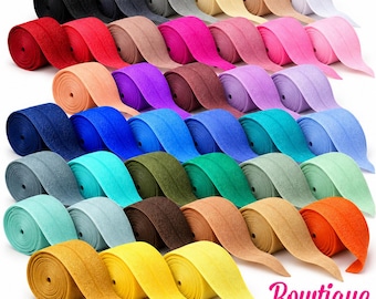 Könnte beinhalten: Eine Sammlung von elastischen Stoffbändern in einer breiten Farbpalette, darunter Schwarz, Grau, Weiß, Rot, Pink, Lila, Blau, Grün, Orange und Gelb. Der Text Bowtique EMILEE ist unten in Pink und Schwarz aufgedruckt.