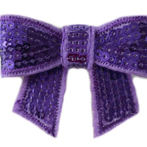 Puede incluir: Un lazo morado con lentejuelas. El lazo est&aacute; hecho de terciopelo y tiene un acabado brillante.