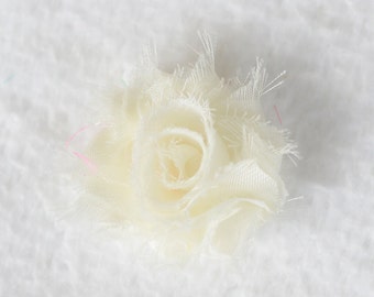 May include: A delicate, off-white fabric flower with a ruffled texture. The flower is made of multiple layers of fabric, creating a soft and romantic look.