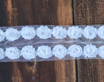 May include: White fabric rose trim with a sheer mesh backing. The trim features two rows of white fabric roses.