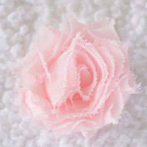 May include: A delicate pink fabric flower with ruffled edges. The flower is made of soft, sheer fabric and has a layered, rosette-like design.
