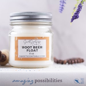 May include: A clear glass jar candle with a silver lid. The label is orange and says "Sweet Scents-ible Candle Co. Root Beer Float 8 oz. sweetscents-ible.com"