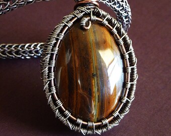 May include: A silver wire wrapped pendant featuring a tiger's eye gemstone. The pendant is oval shaped and has a copper wire accent at the top.