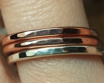 May include: Three stacked rings on a finger. The top two rings are copper and the bottom ring is silver.