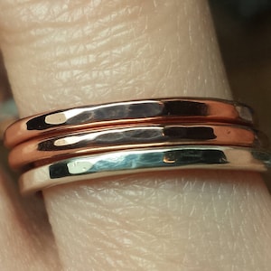 May include: Three stacked rings, one silver and two copper, worn on a finger.