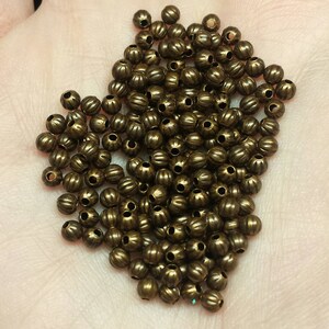 May include: A large pile of small, round, bronze-coloured beads with a textured surface. The beads have a hole in the centre for stringing.