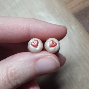 May include: Two white round earrings with a red heart design.