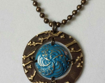 May include: A necklace with a round pendant featuring a blue and gold design. The pendant is surrounded by a textured bronze ring.