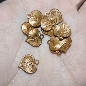 Puede incluir: Un grupo de abalorios de metal de color dorado en forma de hoja con un diseño detallado. Los abalorios tienen forma de corazón con un patrón de hoja.