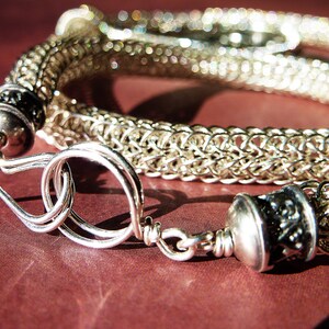 May include: A silver chainmail bracelet with a decorative clasp. The bracelet is made of small, interconnected metal rings.