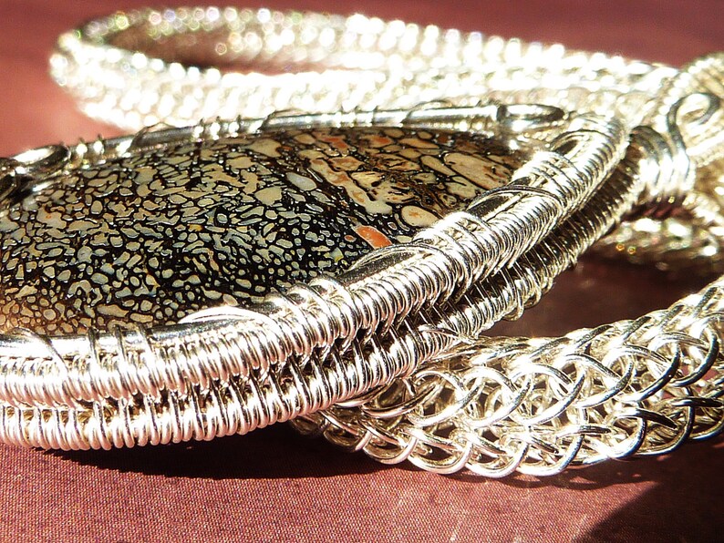 May include: A silver wire wrapped pendant featuring a black and white patterned stone. The pendant is attached to a silver chain.