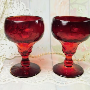 May include: Two red glass goblets with a cut glass design. The goblets have a wide bowl and a tall stem with a round base.