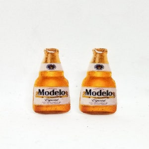 May include: Two miniature Modelo Especial beer bottles with gold foil tops and white labels. The labels display the brand name and logo. The bottles are set against a white background.