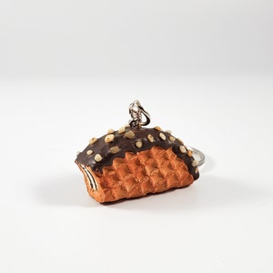 May include: A chocolate-covered waffle keychain with white sprinkles. The keychain is made of polymer clay and has a realistic look.