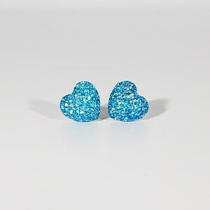 K&ouml;nnte beinhalten: Ein Paar blaue herzf&ouml;rmige Ohrringe mit Glitzer.