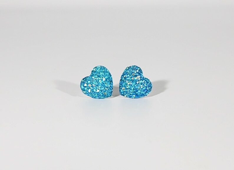 K&ouml;nnte beinhalten: Ein Paar blaue herzf&ouml;rmige Ohrringe mit Glitzer.