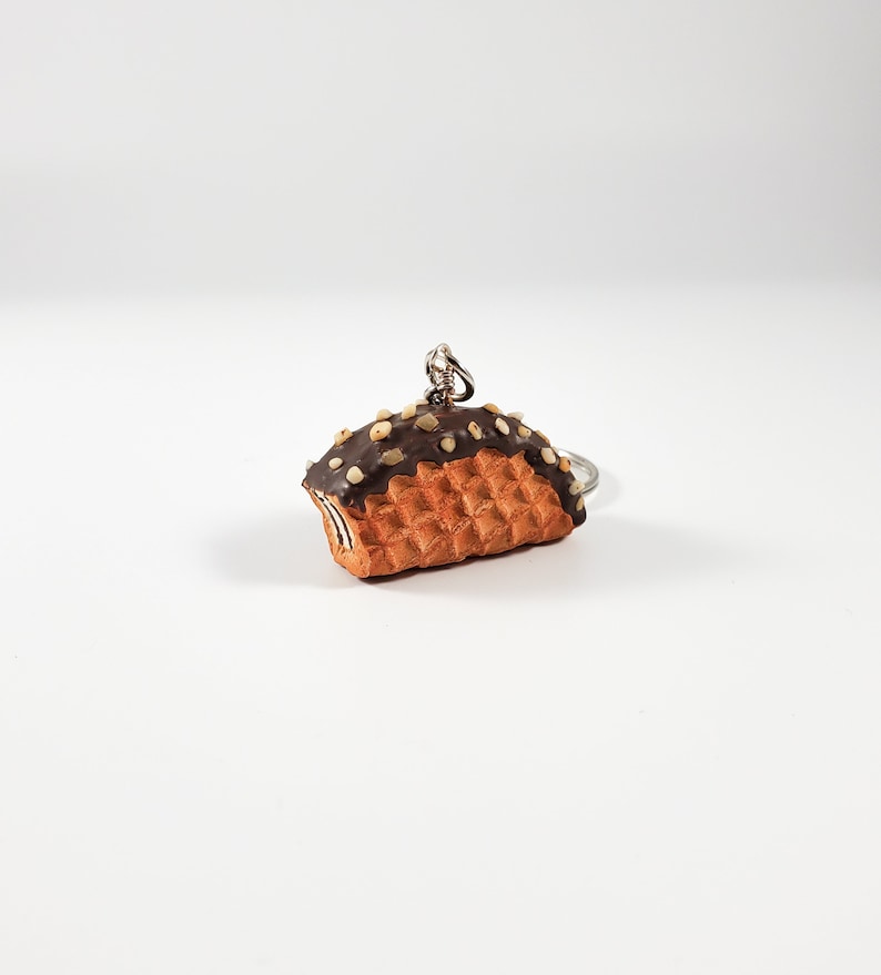 May include: A chocolate-covered waffle keychain with white sprinkles. The keychain is made of polymer clay and has a realistic look.