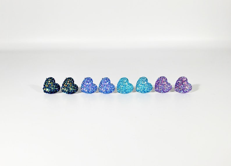 K&ouml;nnte beinhalten: Ein Set mit acht herzf&ouml;rmigen Ohrringen mit Glitzer. Die Ohrringe sind in Blaut&ouml;nen, Lila und T&uuml;rkis.
