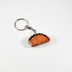 May include: A silver key chain with a chocolate-covered waffle keychain charm. The waffle is a light brown color and has a chocolate drizzle on top.