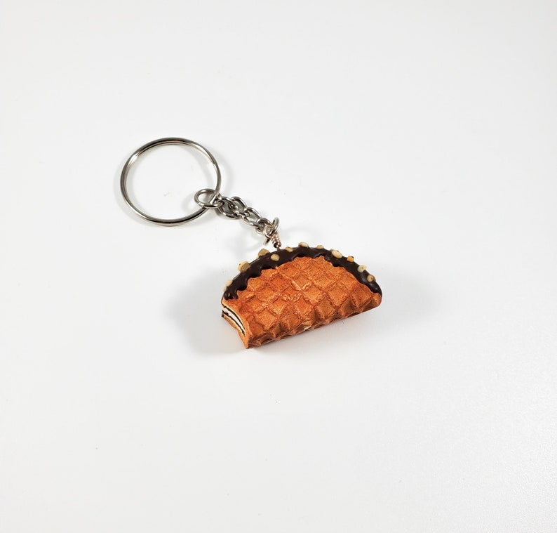 May include: A silver key chain with a chocolate-covered waffle keychain charm. The waffle is a light brown color and has a chocolate drizzle on top.