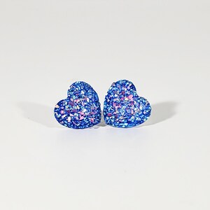 K&ouml;nnte beinhalten: Ein Paar blaue herzf&ouml;rmige Ohrringe mit schimmerndem Glitzer.