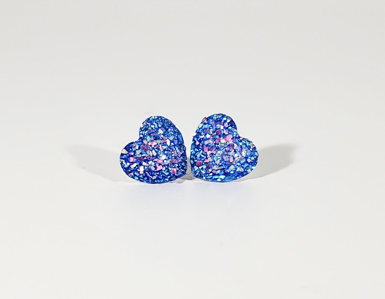 K&ouml;nnte beinhalten: Ein Paar blaue herzf&ouml;rmige Ohrringe mit schimmerndem Glitzer.