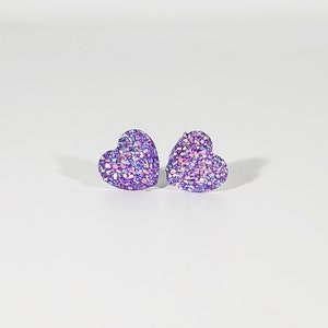 K&ouml;nnte beinhalten: Ein Paar violette herzf&ouml;rmige Ohrringe mit schimmerndem Glitzer.
