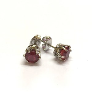 May include: A pair of silver stud earrings with a red gemstone in the centre of each earring.
