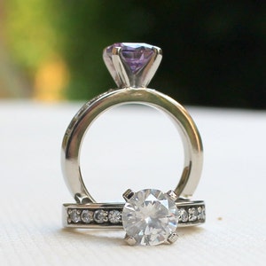 May include: A silver ring with a large, clear round diamond and a smaller purple gemstone set in a silver band.