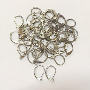 May include: A pile of silver-toned earring hooks. The hooks are made of metal and have a spring-loaded clasp. There are two individual hooks in the foreground.