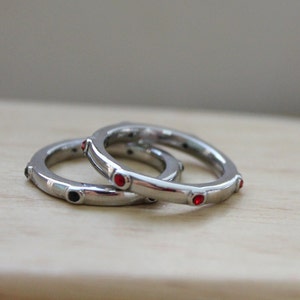 May include: Two silver rings with red and black gemstones. The rings are stacked on top of each other.