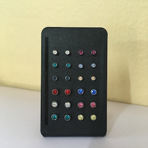 May include: A black display case with 24 small round earrings with various colored rhinestones. The earrings are arranged in rows of four.