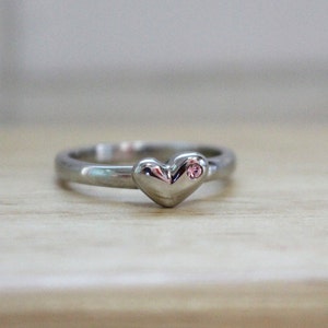 May include: A silver ring with a heart-shaped design and a small pink gemstone.