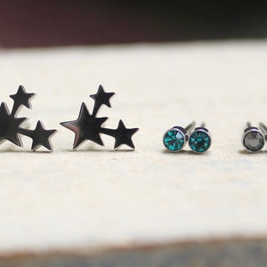 May include: Two pairs of earrings. One pair features a cluster of five silver stars. The other pair features two small round blue gemstones.