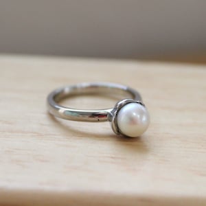 May include: A silver ring with a single white pearl set in the center.