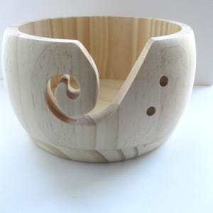 May include: A natural wood yarn bowl with a carved out swirl design and two holes on the side.