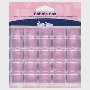 May include: A clear plastic bobbin box with a hinged lid, designed to hold 25 sewing machine bobbins. The box has a grid of individual compartments and is set against a pink background. The text "Bobbin Box" is visible.