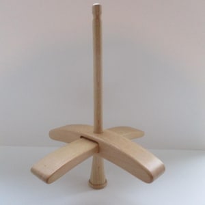 May include: A light-coloured wooden yarn swift, a tool for winding yarn into a skein. The swift has a central vertical post with a cross-shaped base and four curved arms extending outwards. The wood has a natural finish.