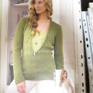 May include: A green knitted sweater with a deep V-neck and long sleeves. The sweater is made with a textured yarn and has a relaxed fit. The model is wearing the sweater with white trousers and a necklace.