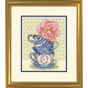 May include: Framed cross-stitch art showing three stacked teacups with blue and white patterns, topped with a pink flower. The artwork is set against a patterned background and framed in gold, with a navy blue border.
